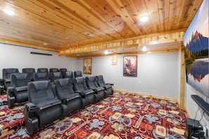 A room with wooden ceiling, black leather chairs, a patterned carpet, and a large TV screen. - Make Lasting Memories: Pool, Hot Tub, Games & MORE (Pigeon Forge)