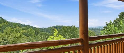 A wooden balcony with a view of a forested landscape.