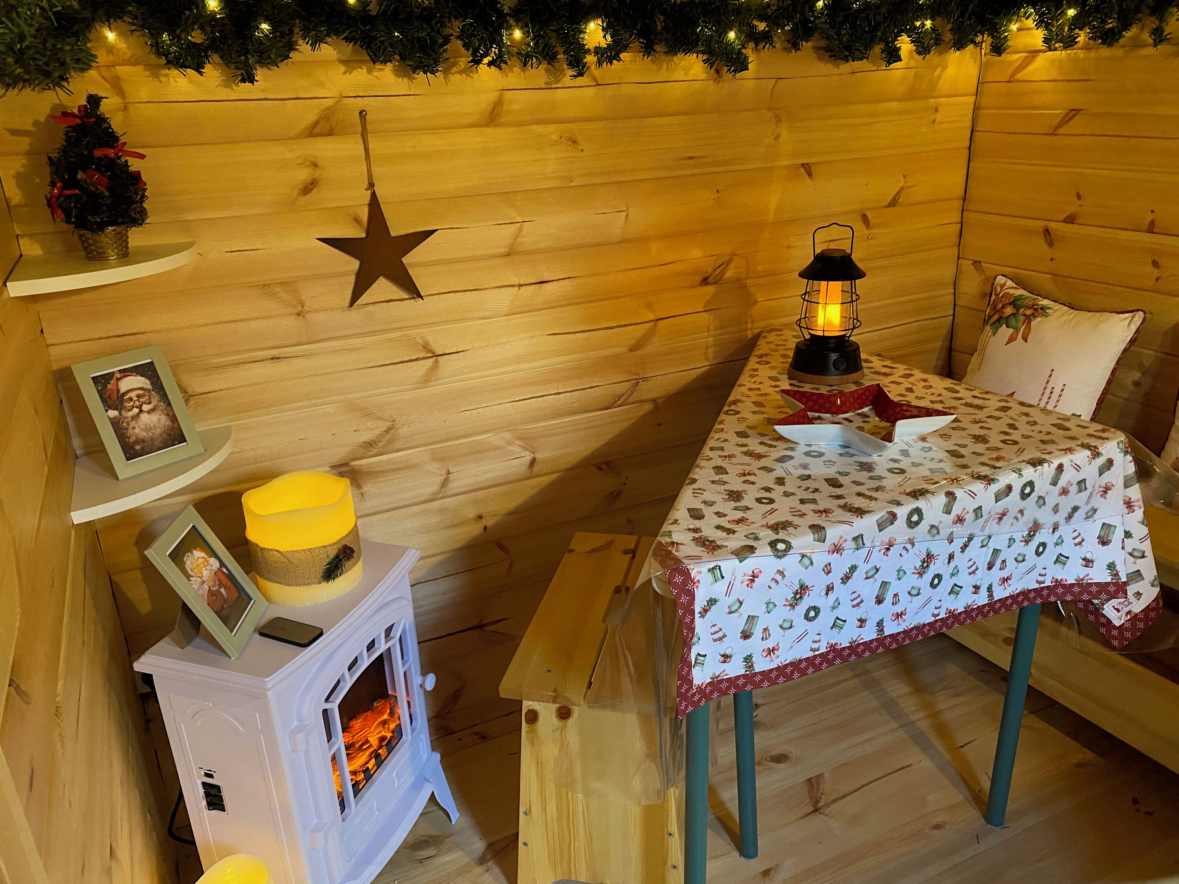 A cozy room with a wooden interior, a small table with a festive tablecloth, a lit lantern, and a star decoration on the wall.