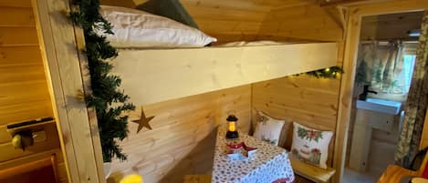 A cozy cabin interior with a bunk bed, a small table with a lantern, and a window with curtains.