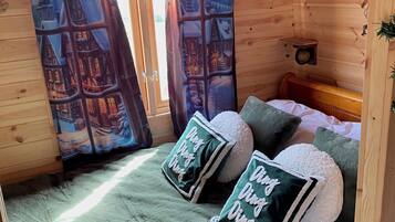 A cozy room with a bed, green pillows, a window with a view of a snowy village, and a Christmas tree.