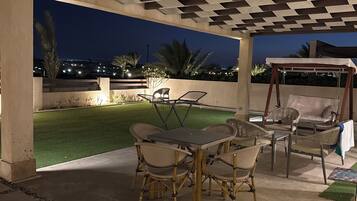 An outdoor patio area with a table and chairs, a swing set, and a view of the city at night.