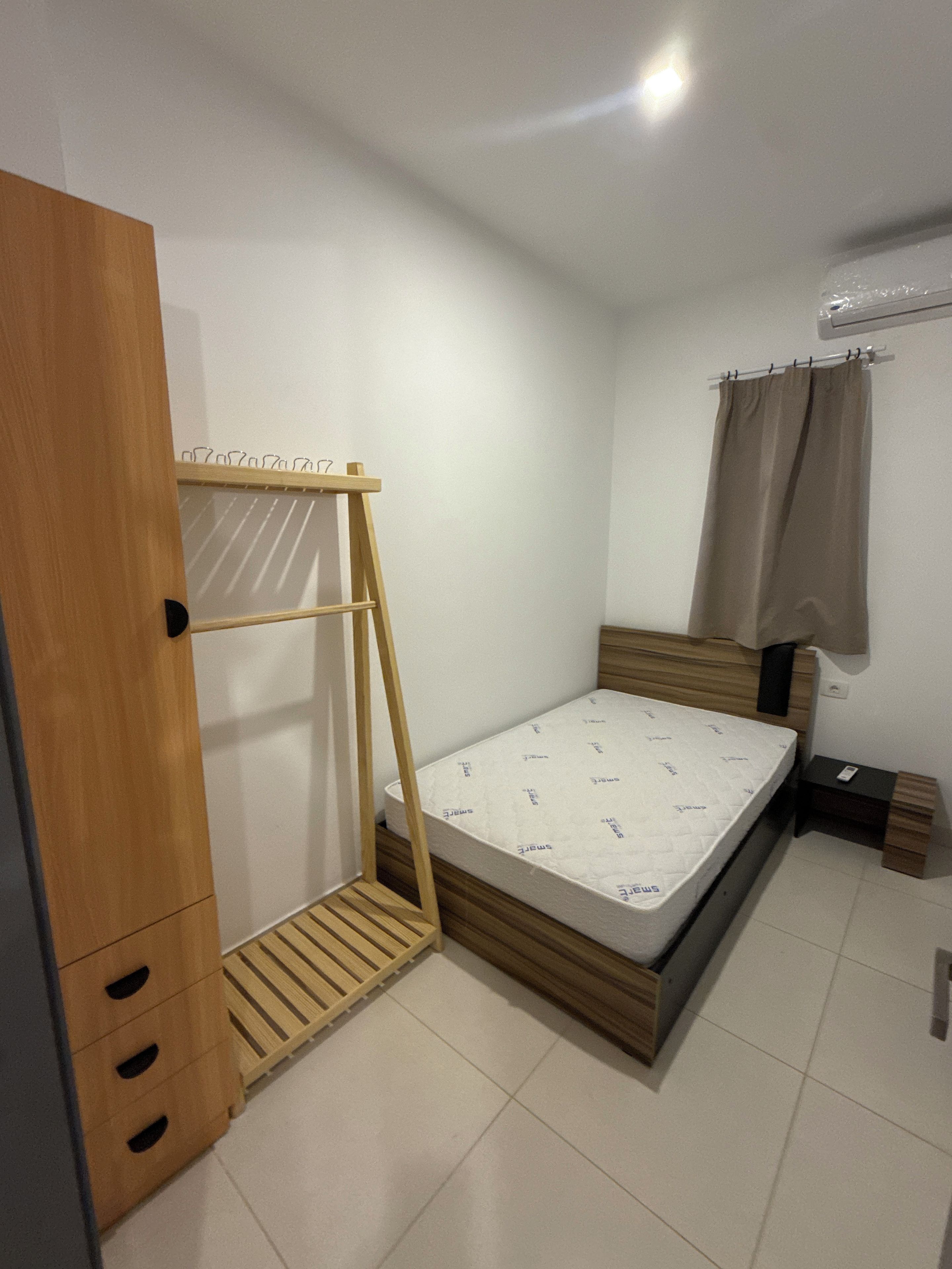A bedroom with a wooden wardrobe, a bed with a mattress, a wooden ladder, a small bedside table, and a curtain.