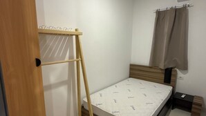 Een slaapkamer met een houten garderobe, een bed met matras, een houten trap, een klein nachtkastje en een gordijn.