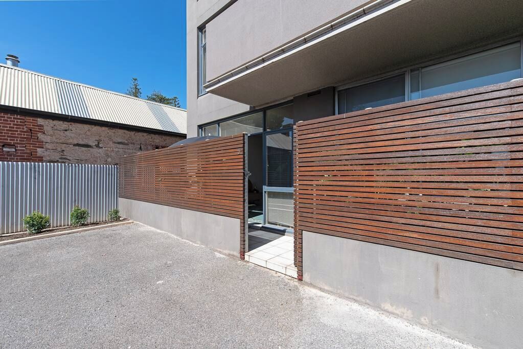 A modern building with a concrete facade, a wooden slatted wall, and a metal fence.