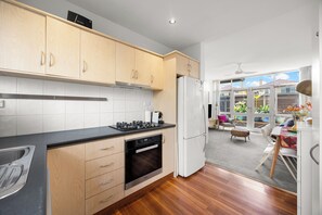 A modern kitchen with wooden cabinets, a built-in oven, and a refrigerator. - Glee Tides By the Beach Indoor outdoor Lifestyle (Glenelg East)