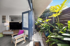 A modern living space with a sofa, a TV, and a dining area. - Glee Tides By the Beach Indoor outdoor Lifestyle (Glenelg East)