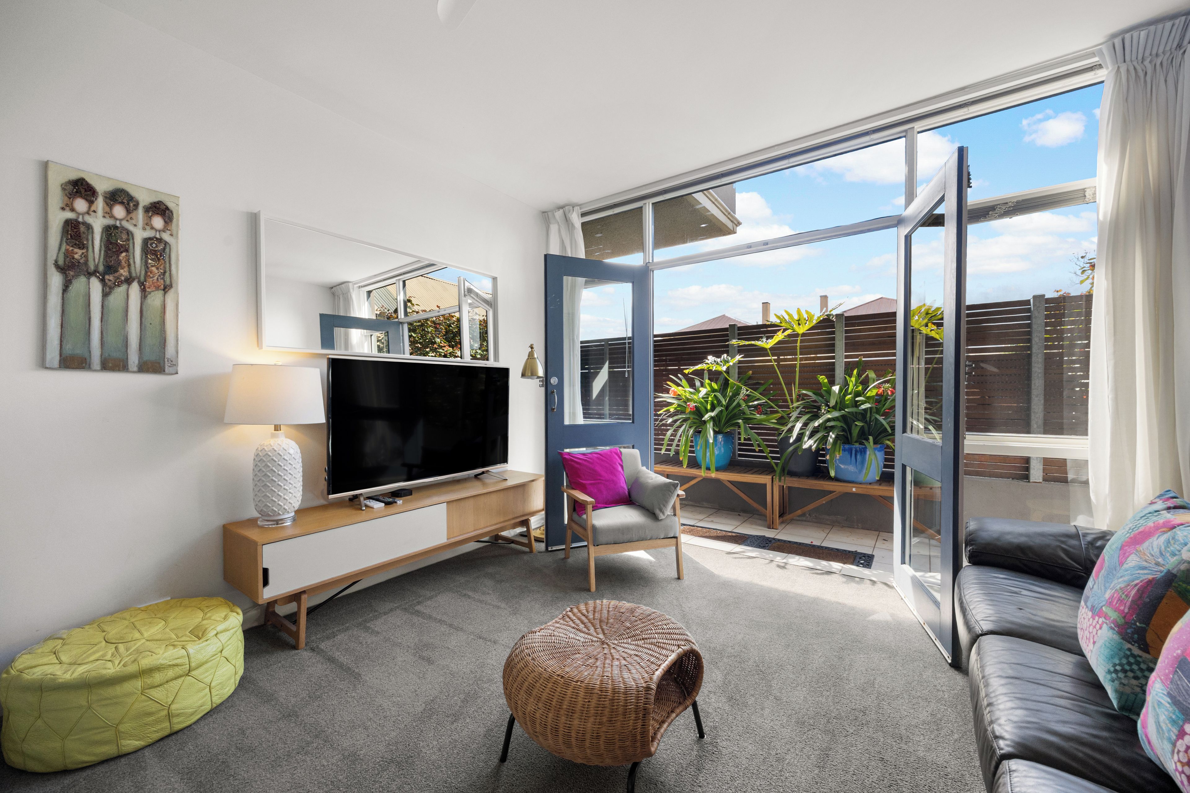 Een moderne woonkamer met een flatscreen televisie, een bank, een fauteuil, een bijzettafeltje en een groot raam met uitzicht op de omgeving.