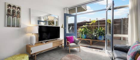 Una sala de estar moderna con una televisión de pantalla plana, un sofá, una silla, una mesita y un ventanal con vistas al exterior.