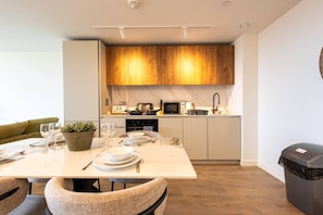 A modern kitchen with wooden cabinets, a dining table set for two, and a small potted plant. - Birmingham City Retreat No 154 (Birmingham)