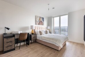 A bedroom with a bed, a desk, a chair, a bedside table with lamps, and a large window offering a view. - Birmingham City Retreat No 154 (Birmingham)