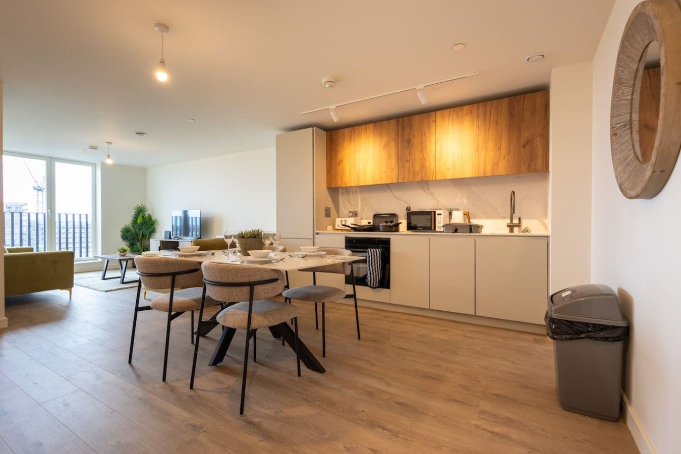Eine moderne Küche mit Holzausstattung, ein Essbereich mit rundem Tisch und Stühlen sowie ein Blick auf die Stadt durch große Fenster.