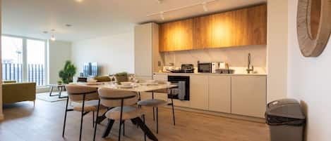 Eine moderne Küche mit Holzausstattung, ein Essbereich mit rundem Tisch und Stühlen sowie ein Blick auf die Stadt durch große Fenster.