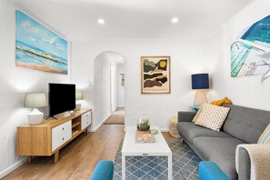 A modern living room with a flat-screen TV, a grey sofa, a coffee table, and artwork on the walls. - Glenelg Bliss Charming Escape for Beachside Fun (Glenelg)