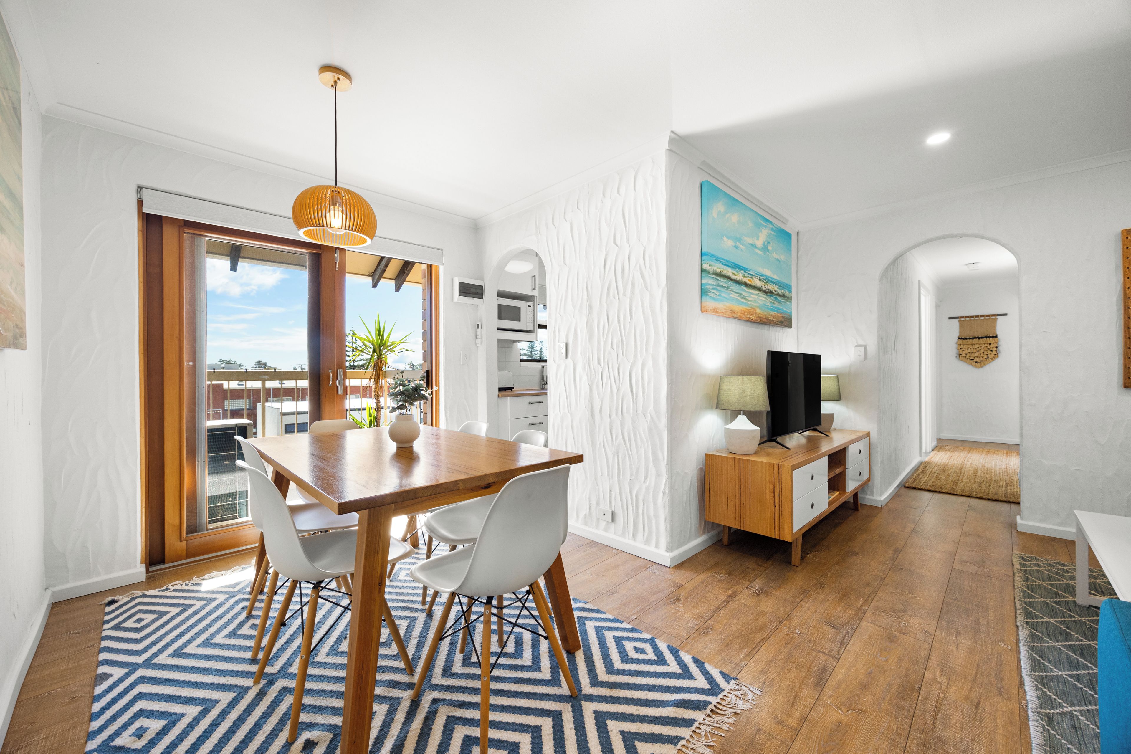 Een moderne woonkamer met een houten eettafel, witte stoelen, een televisie en een schilderij aan de muur.