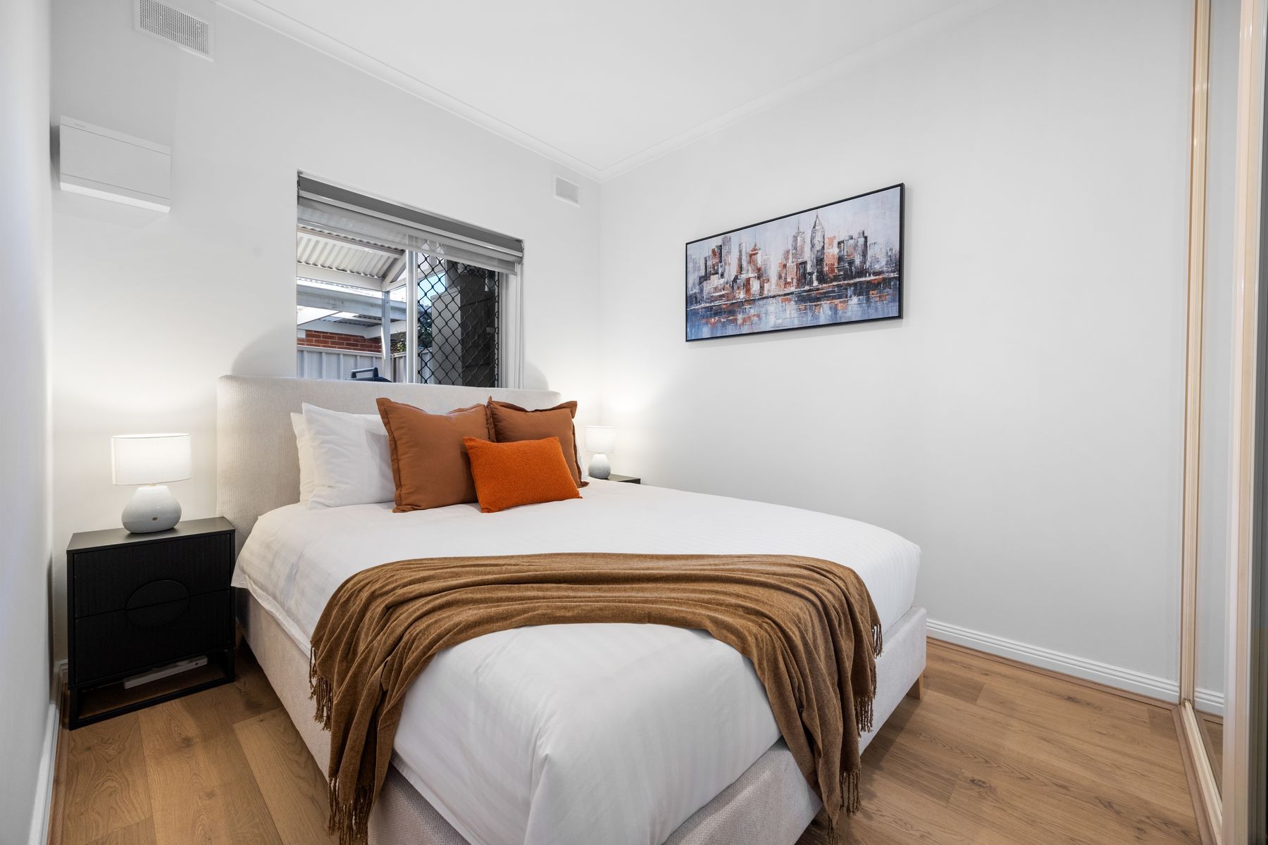 Une chambre à coucher avec un lit, une table de chevet, une fenêtre et un tableau représentant un paysage urbain accroché au mur.