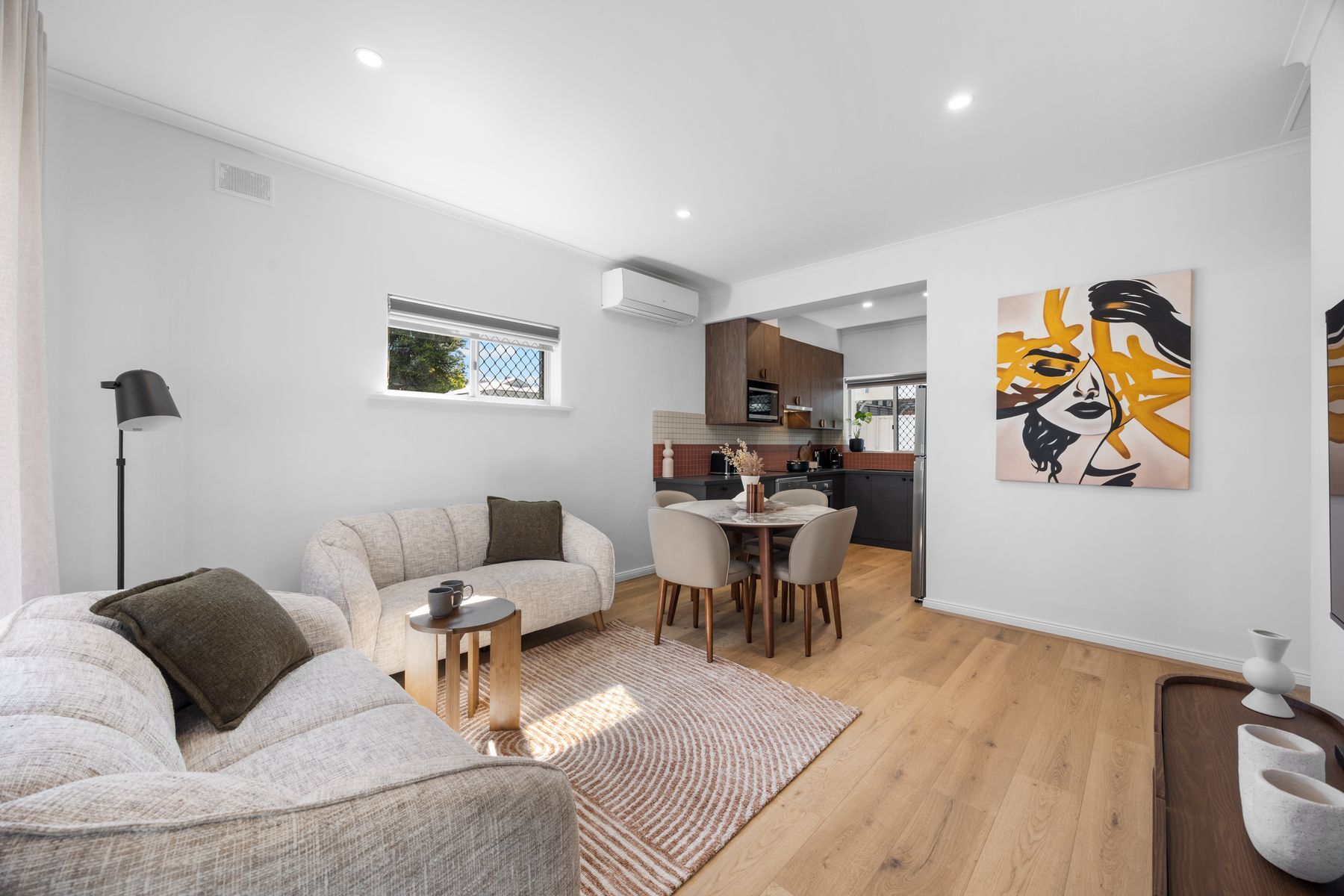 Een moderne woonkamer met een bank, een salontafel en een eethoek met stoelen. In de achtergrond is een keuken zichtbaar.