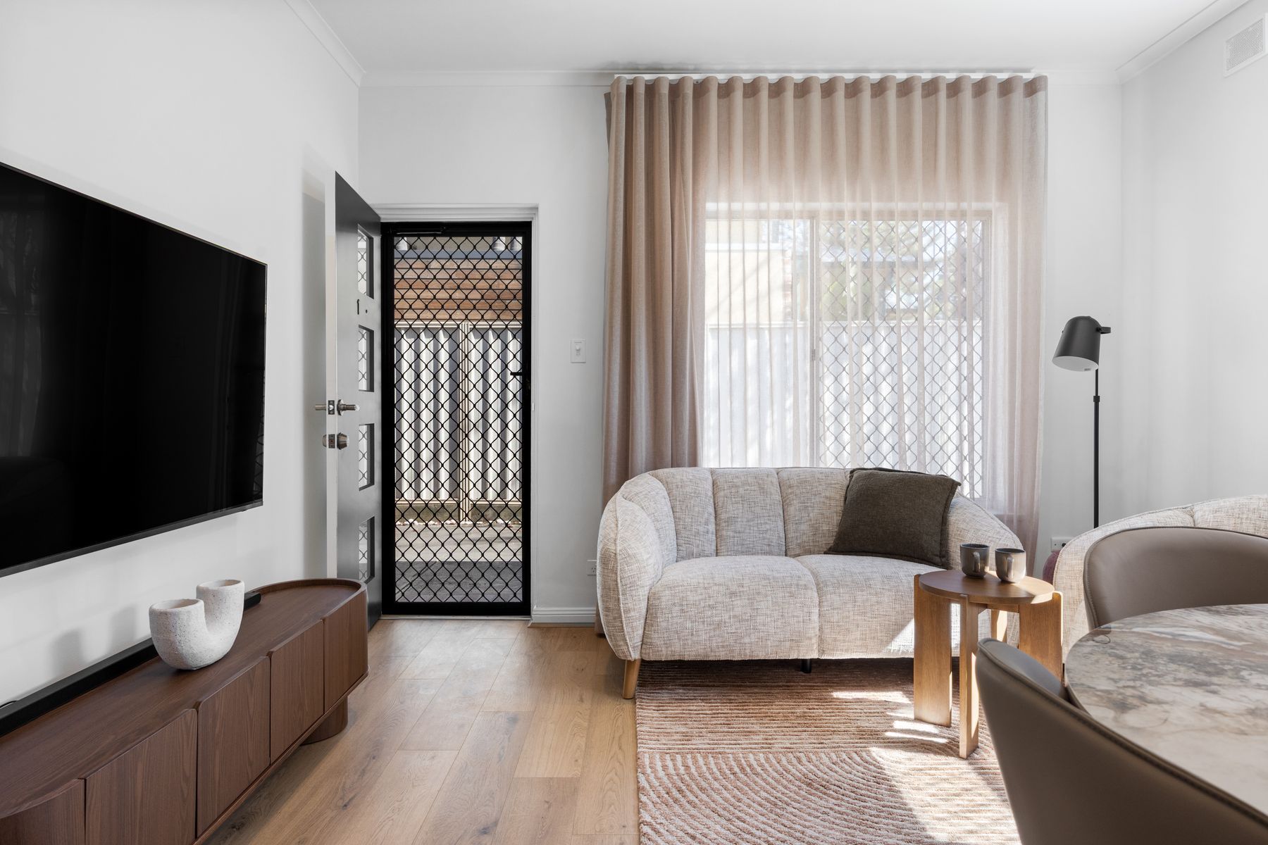 A modern living room with a flat-screen TV, a sofa, a coffee table, and a patterned rug.