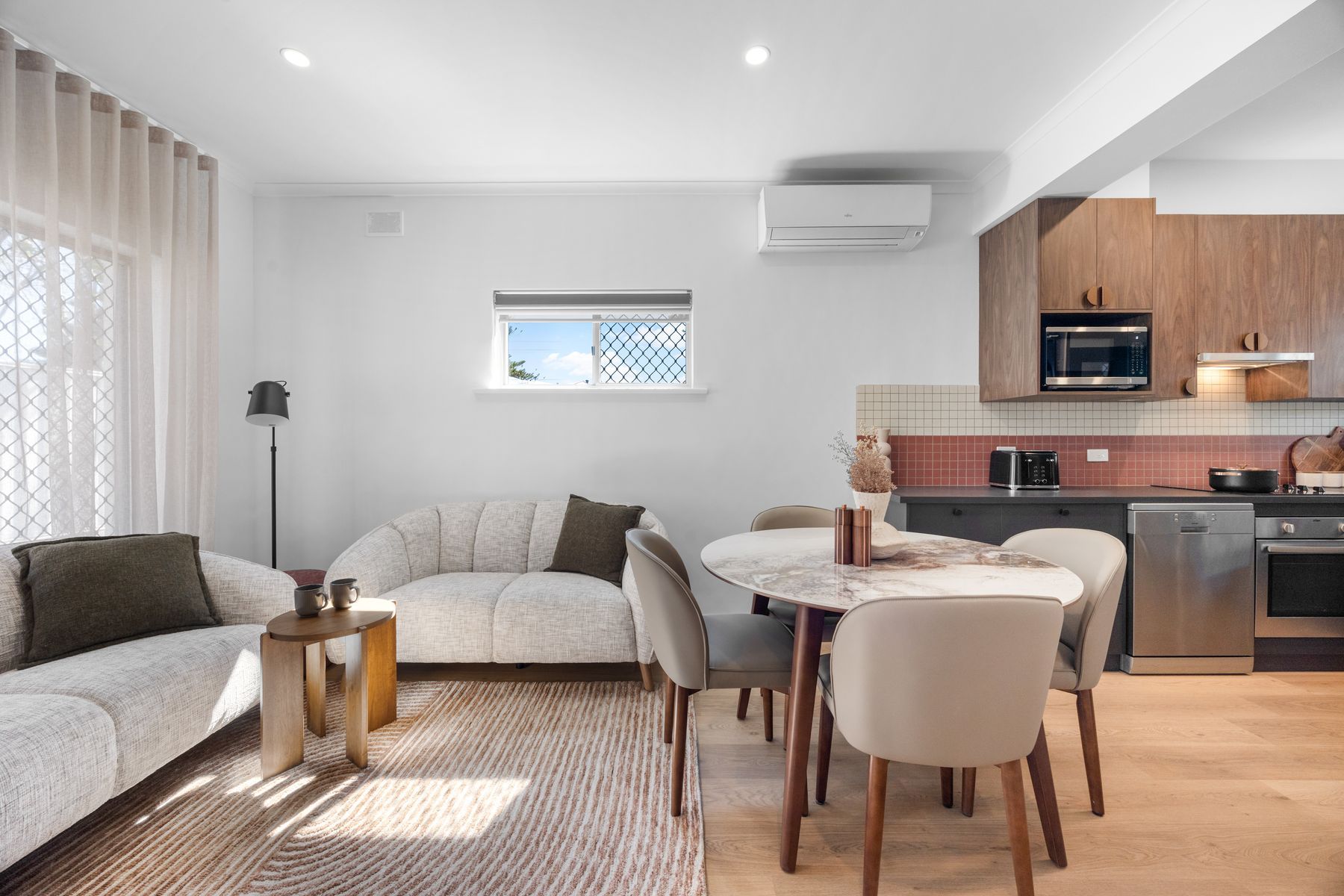 Un espace de vie moderne comprenant un canapé, une table à manger, des chaises et un coin cuisine équipé d’appareils électroménagers.
