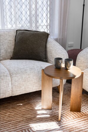 A living room with a sofa, a round wooden coffee table, and a patterned rug. - Broadway Hideaway Laid Back Days near the Beach (Glenelg East)