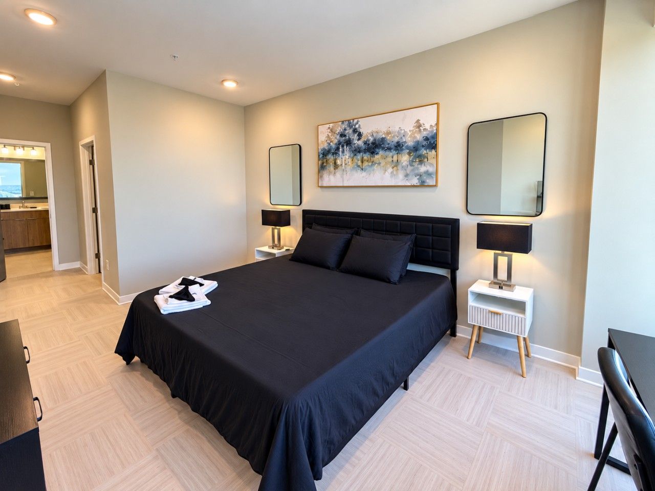 Een moderne hotelkamer met een groot bed, nachtlampjes, een schilderij aan de muur en uitzicht op de keuken.
