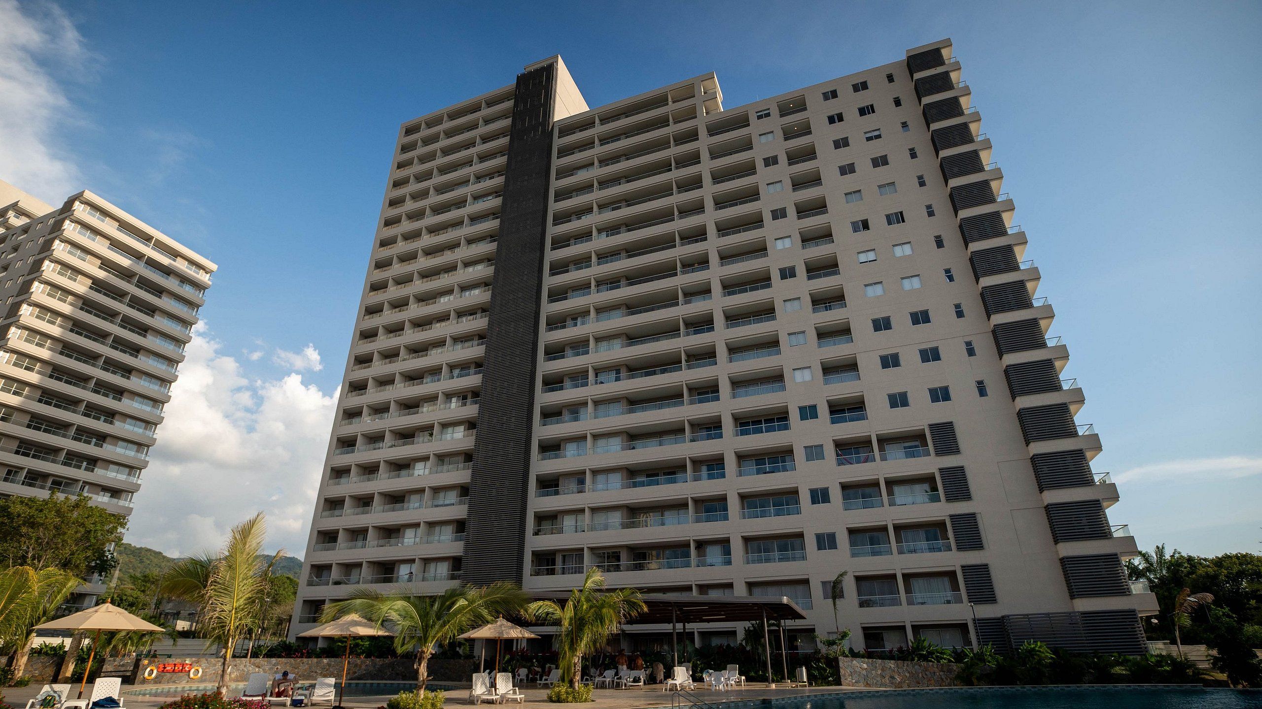 Hotel alt, amb múltiples balcons, zona de piscina amb gandules i cel serena.