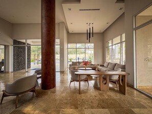 A spacious lobby with a large wooden column, a seating area with sofas and a coffee table, and large windows offering views of the outside. - Suite santa marta 614 - T1 (Santa Marta)