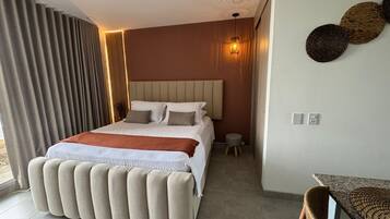Un dormitorio moderno con una cama grande, un taburete pequeño y una silla de mimbre.