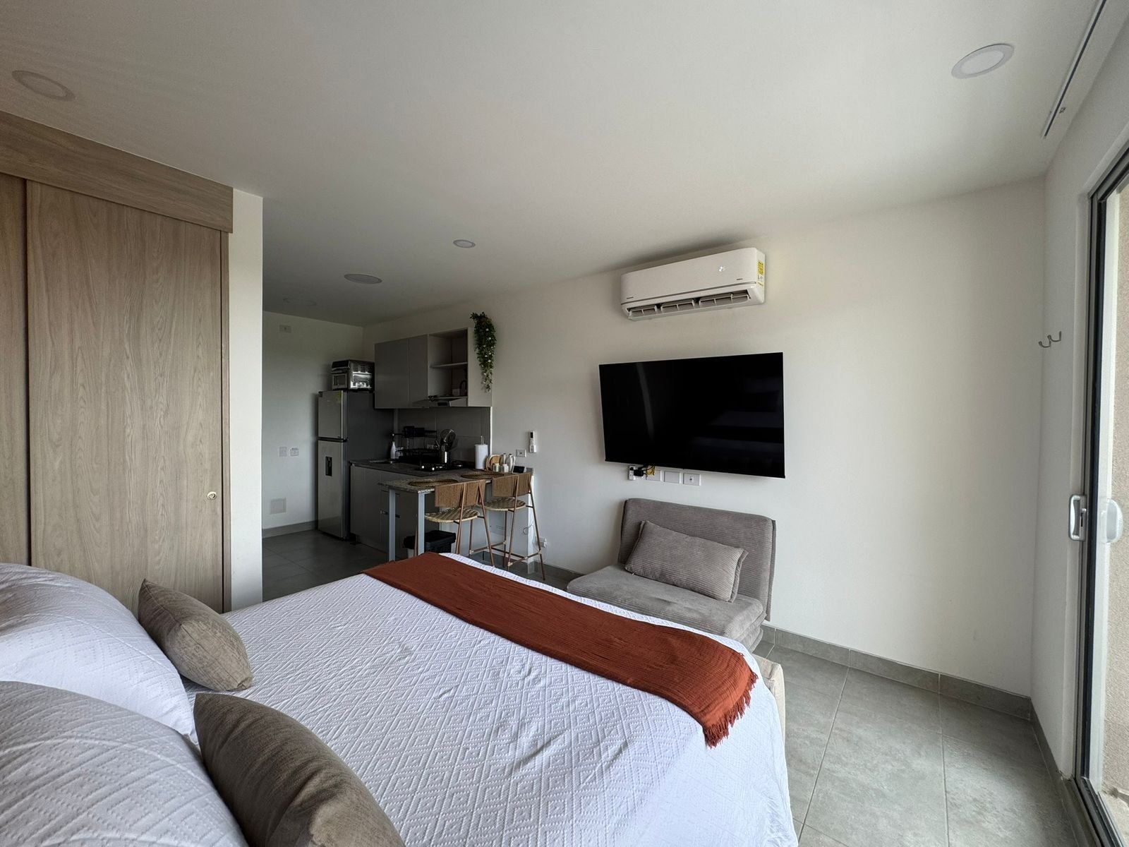 Een moderne hotelkamer met een bed, een televisie, een kitchenette en een schuifdeur.
