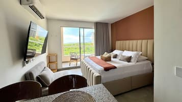 Una habitación de hotel con cama, televisión, balcón con silla y vista a zonas verdes.