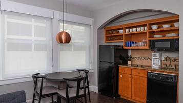A compact kitchen with a refrigerator, microwave, coffee maker, and wooden shelves.