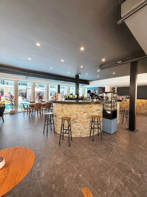 A modern bar area with a stone counter, stools, and a view of the outdoors. - Upscale Playacar Studio w Beach Club & 4 Pools (Playa del Carmen)