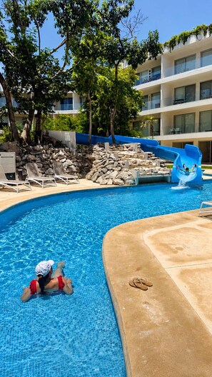 A swimming pool with a water slide, lounge chairs, and a stone wall. - Upscale Playacar Studio w Beach Club & 4 Pools (Playa del Carmen)