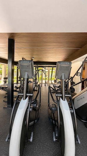 A row of stationary bikes labeled MATRIX in a gym with a wooden ceiling and a view of outdoor greenery. - Upscale Playacar Studio w Beach Club & 4 Pools (Playa del Carmen)