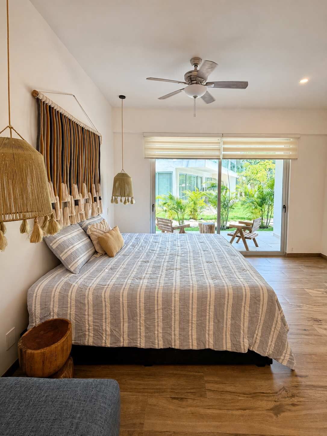 Un dormitorio con cama, ventilador de techo, lámpara colgante y vistas a un patio con mobiliario exterior.