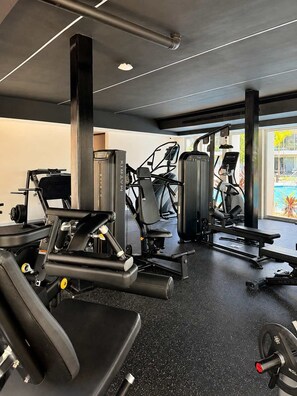 Un gimnasio con varias máquinas de ejercicio, suelo de goma negra y amplias ventanas.