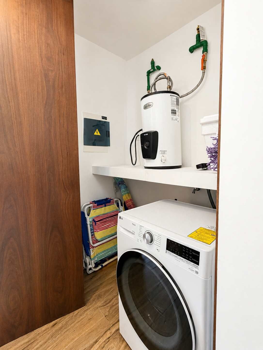 Un cuarto de lavado con lavadora, secadora y calentador de agua sobre un estante blanco.