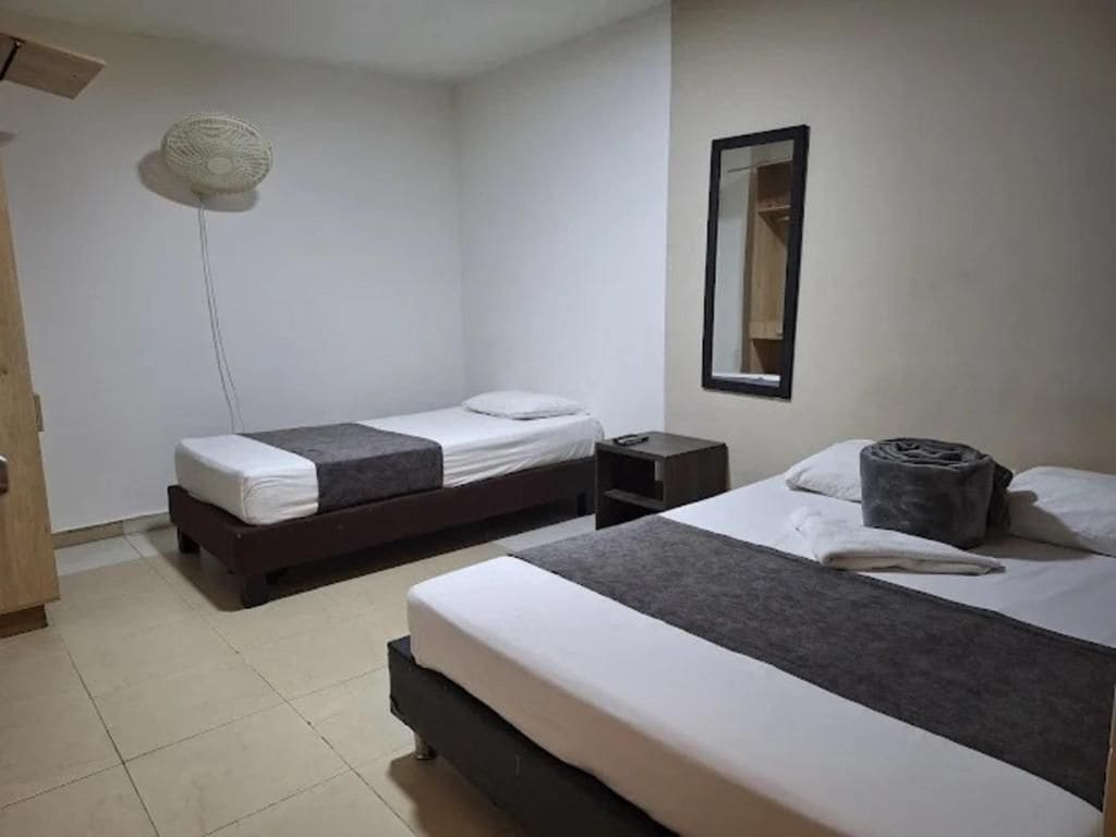 A hotel room with two single beds, a bedside table, a wall-mounted mirror, and a ceiling fan.