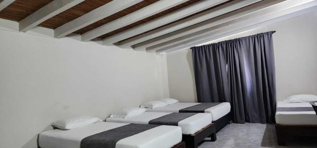 Una habitación de hotel con tres camas dispuestas en fila, una ventana con cortinas y un techo de madera.