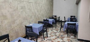 Un restaurante con manteles a cuadros, sillas negras y piso de baldosas de piedra.