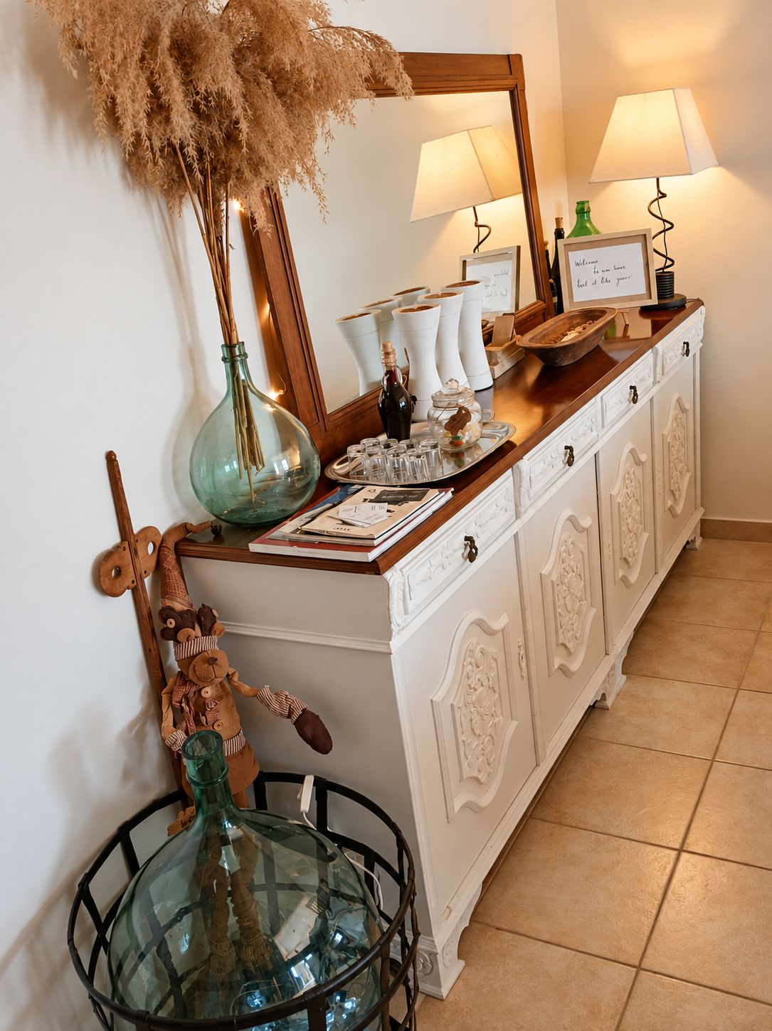 A white cabinet with decorative items, a mirror, and two lamps.