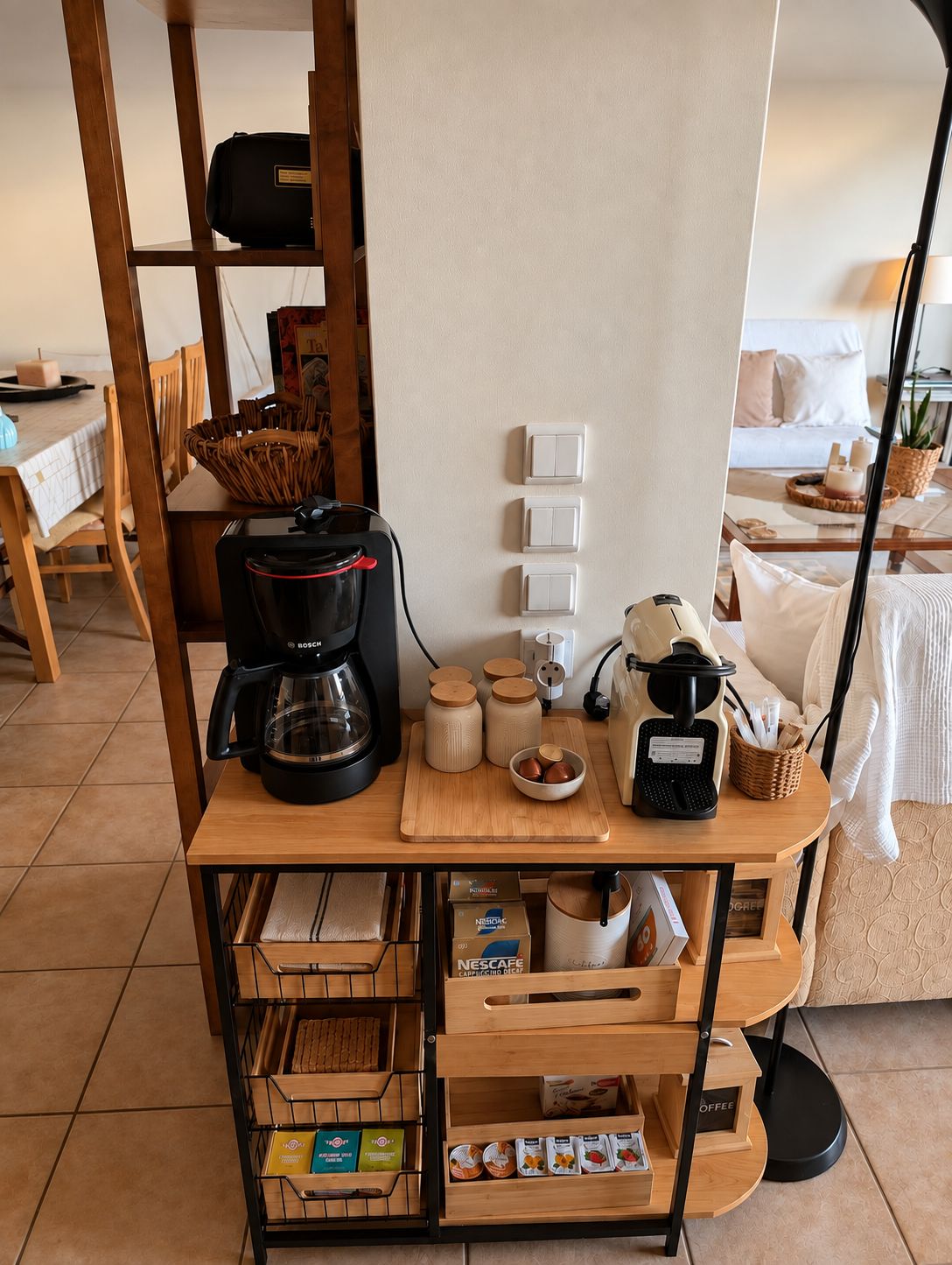 A kitchenette with a coffee maker, jars, and a basket on a wooden table.
