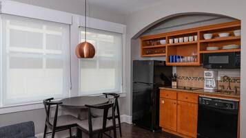 A compact kitchen with a refrigerator, microwave, coffee maker, and wooden shelves.