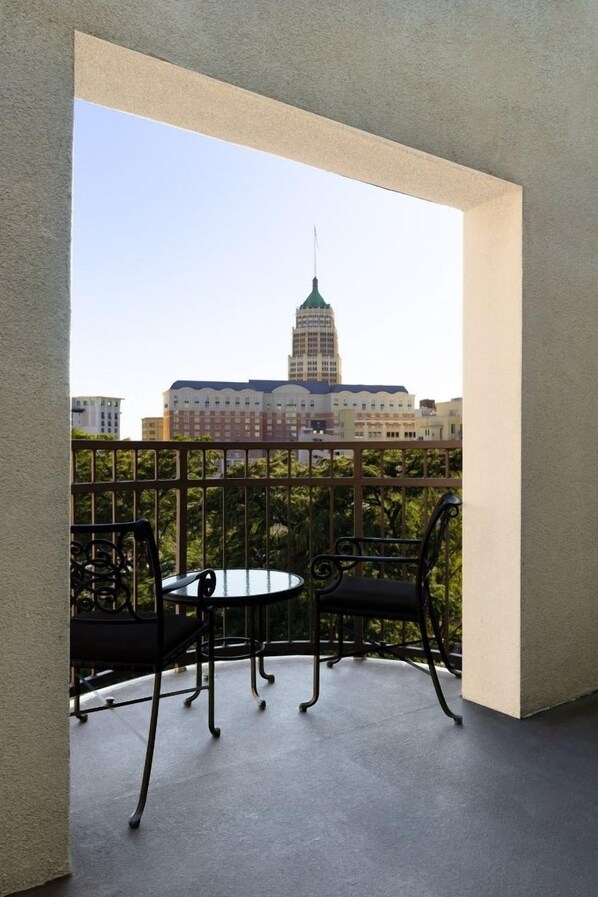 A balcony with two chairs and a table, a metal railing, and a view of a building with a green spire.
