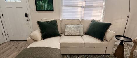 A living room with a beige sofa, two green pillows, a map pillow, a floor lamp, and a patterned rug.