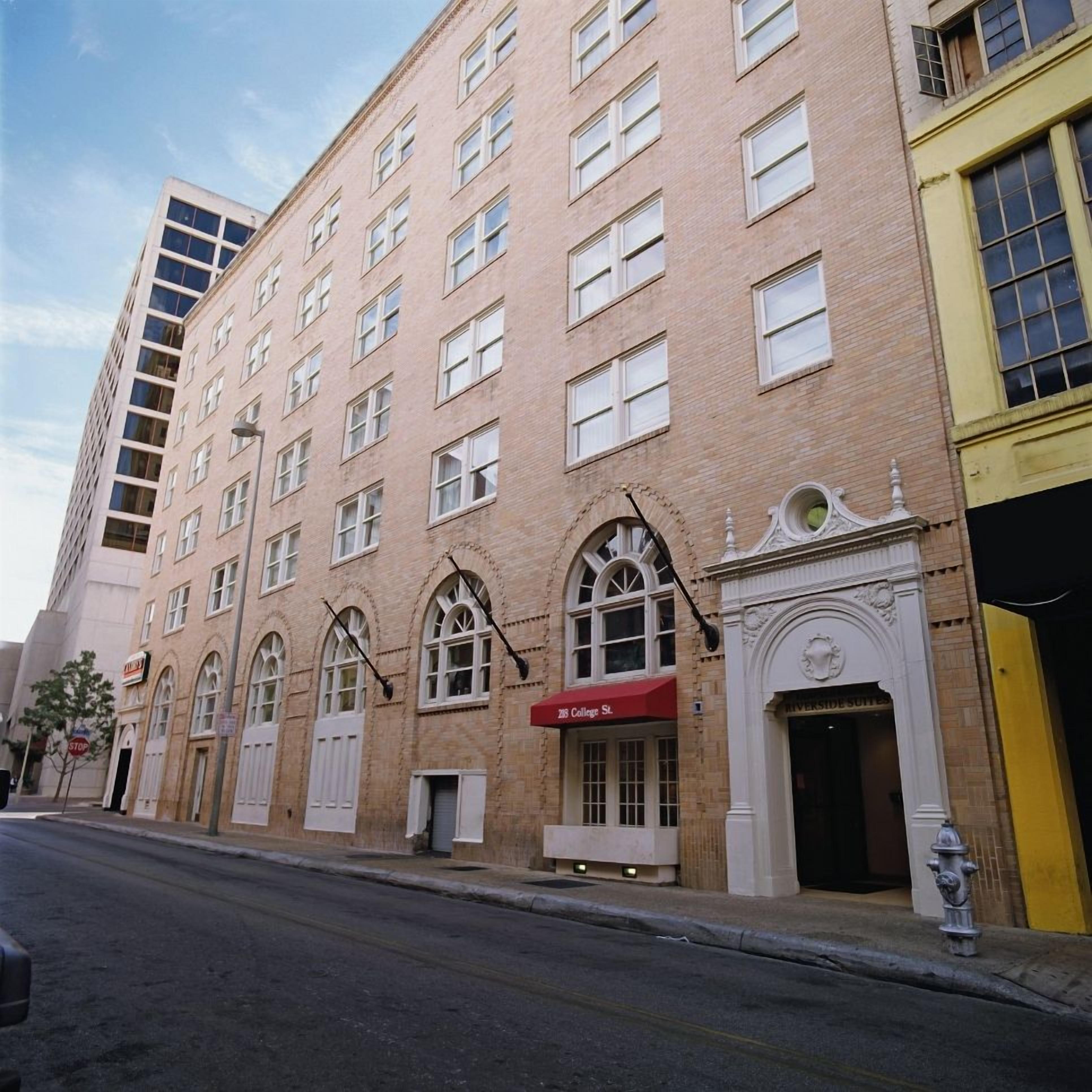 A multi-story building with a red awning labeled '208 College St.' and a sign for 'Riverside Suites.'