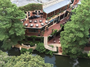 A riverside restaurant with outdoor seating, a bridge, and a building with a brick facade. - San Antonio | Urban Group Retreat | Sun Deck + Downtown | 2BR (San Antonio)