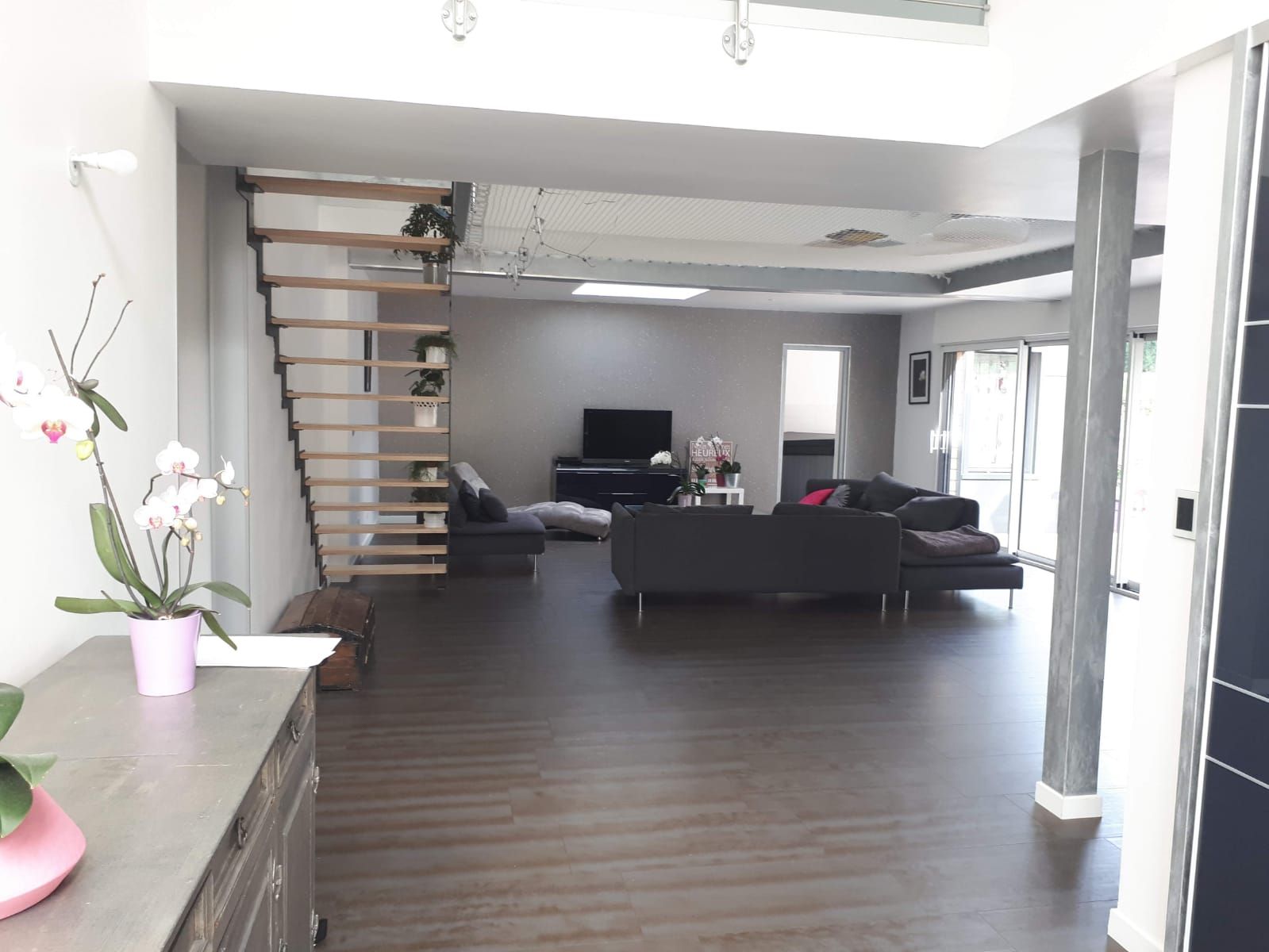 A modern living room with a staircase, a flat-screen TV, and a sofa.