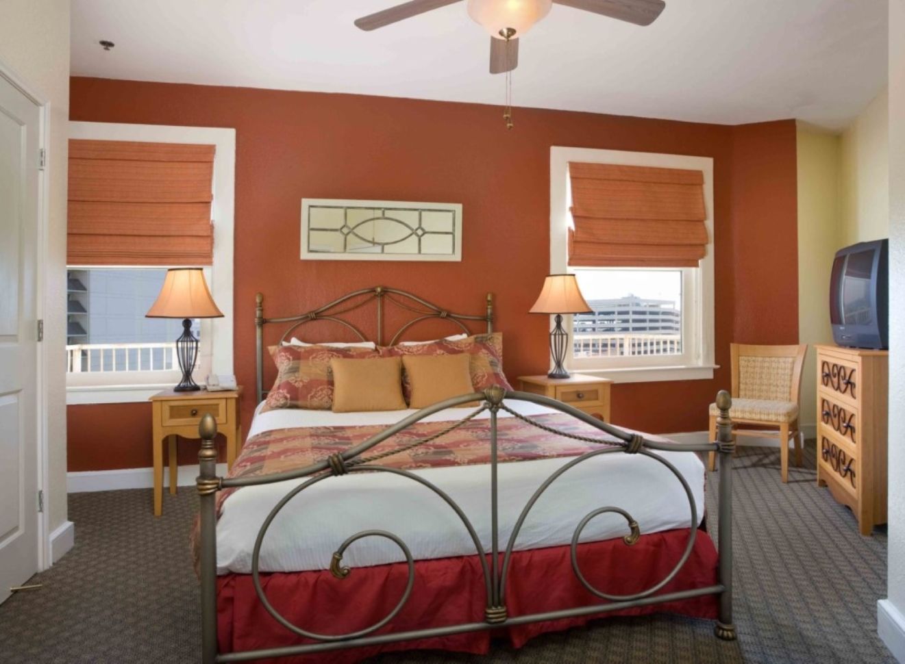 A bedroom with a metal-framed bed, two bedside tables with lamps, a dresser, and a ceiling fan.