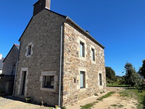 A stone building with a gabled roof, a chimney, and a small garden area with a pathway.